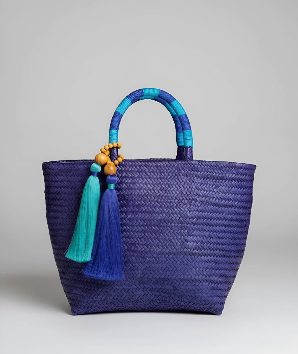 Handwoven Brazilian straw bag in dark blue with subtle purple tones, featuring woven handles, colorful tassels, and artisanal craftsmanship.