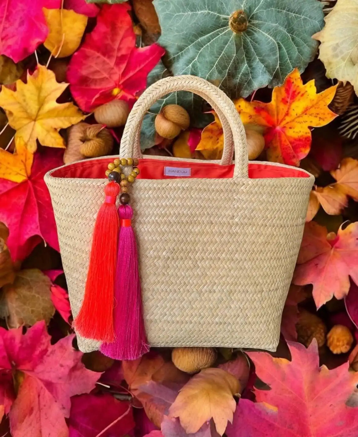 Woven handbag with colorful tassels on a background of autumn leaves and pumpkins.
