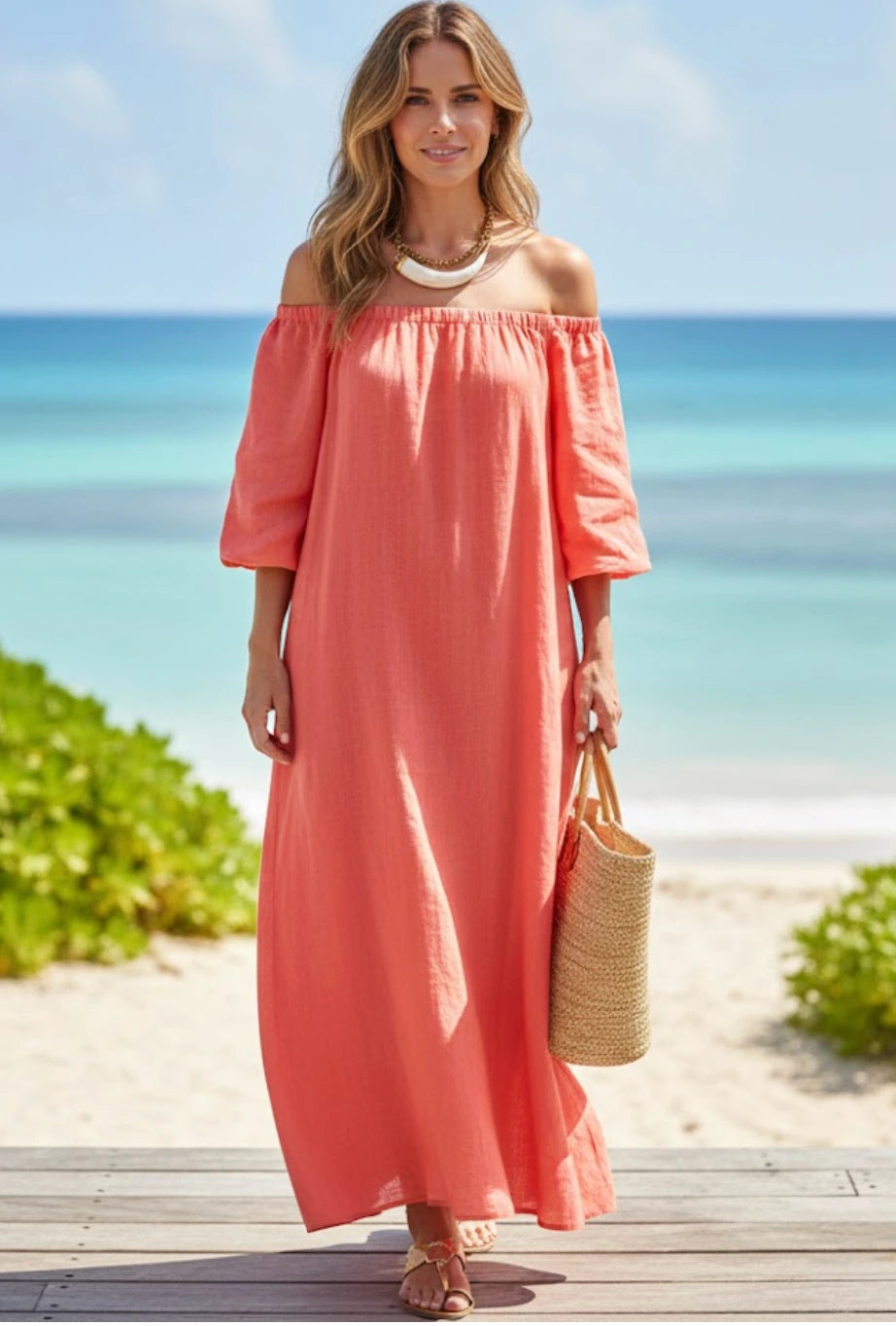 Woman in a coral off-shoulder dress standing on a beach with ocean view wearing a statement necklace.
