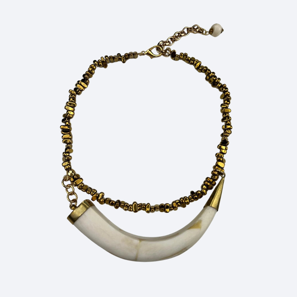 Necklace with gold beaded chain and white horn-like pendant on a white background